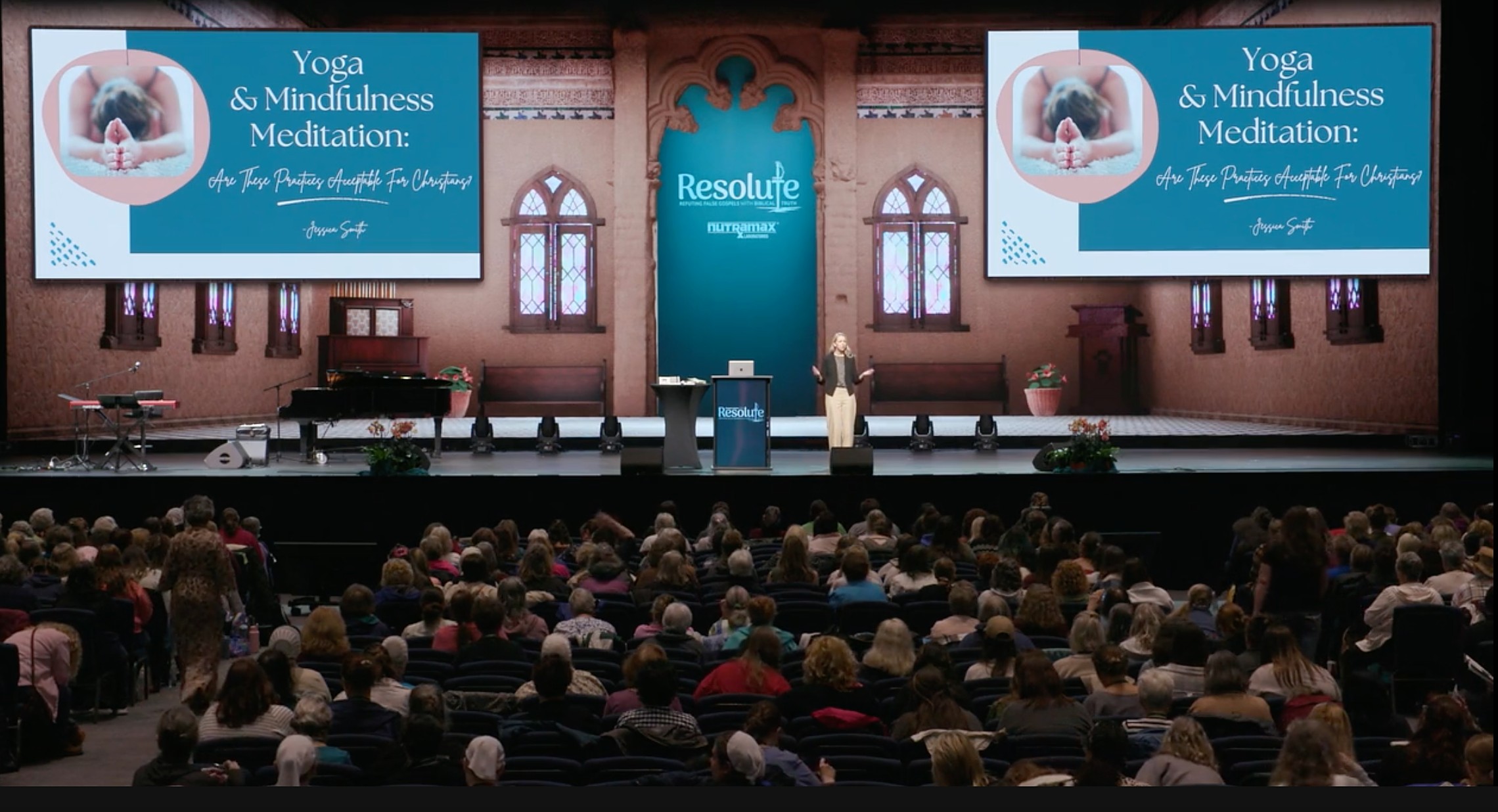 Jessica speaking on stage to a full auditorium